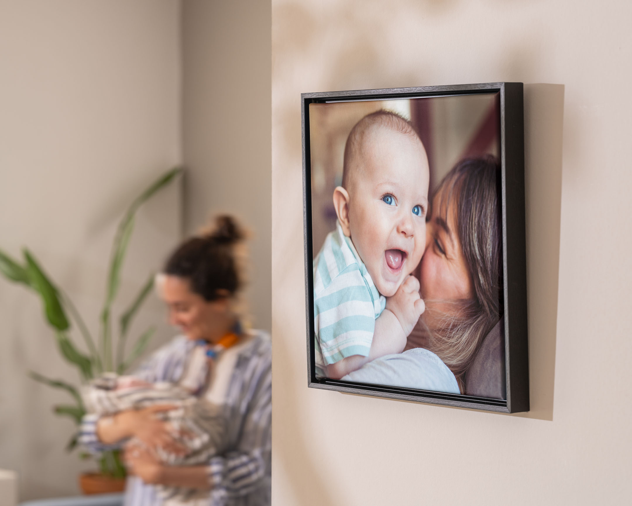 Indrammet fotolærred med en mor, der krammer sin baby, vist på en væg